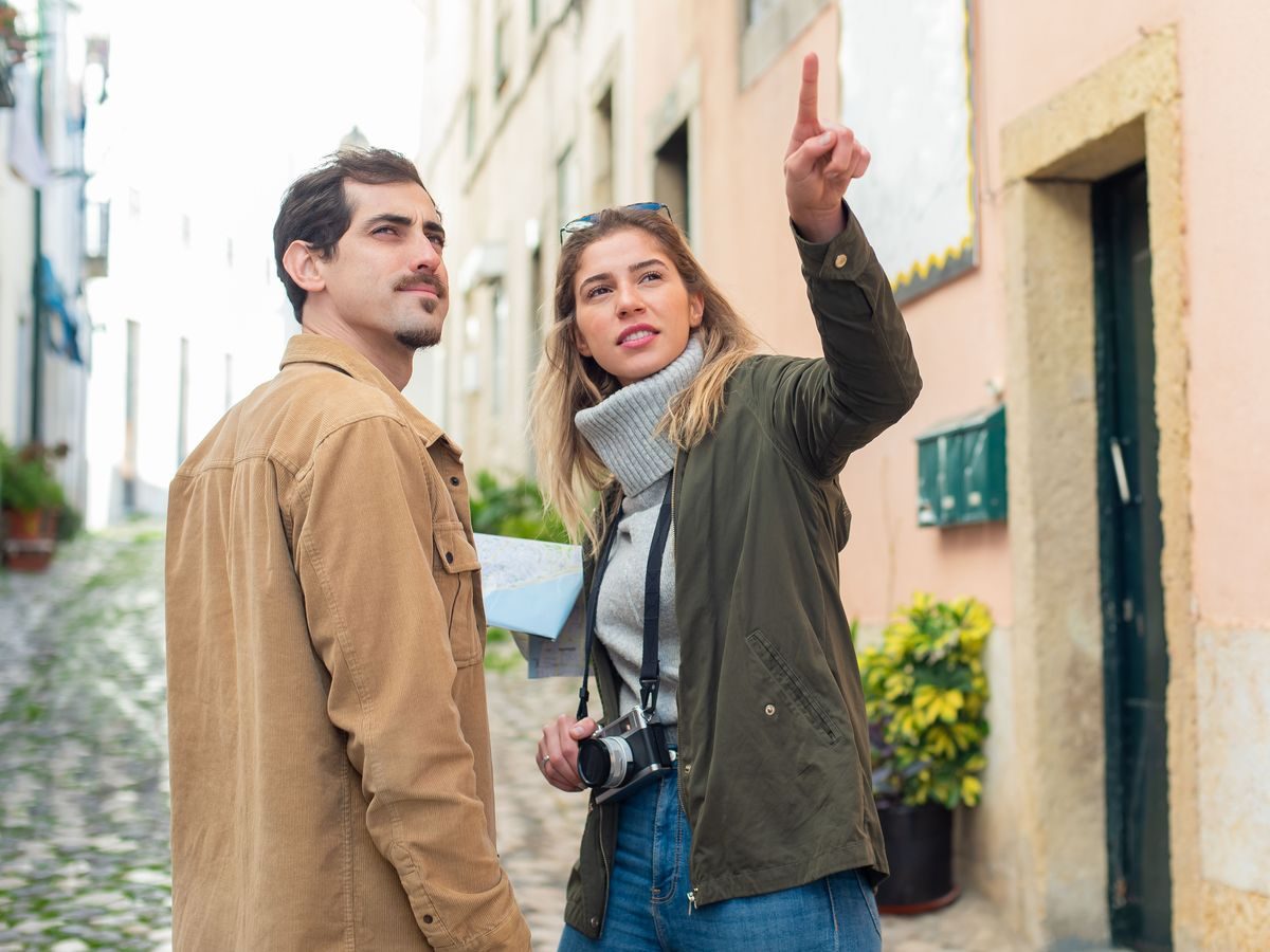 Two travellers on a cobbled street, looking up at the old houses