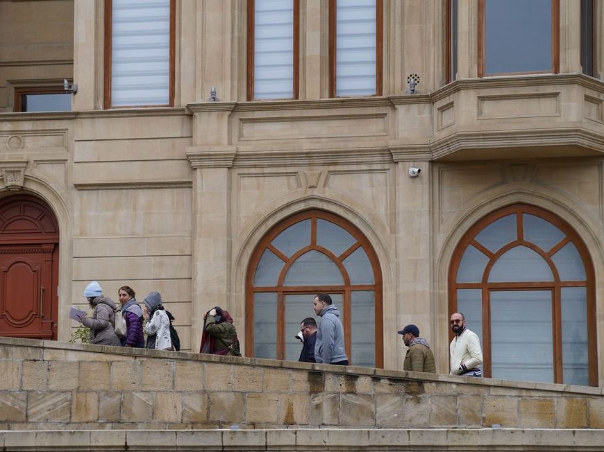 A small group on the terrace of a grand stone building with arched windows